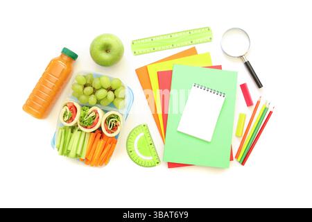 Articoli di cancelleria dai colori vivaci e spuntini freschi disposti su una superficie bianca, che mostrano la preparazione per la sessione di studio o il lavoro di progetto. Le opzioni salutari includono frutta e verdura. Foto Stock
