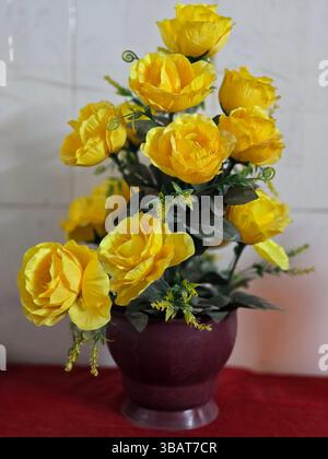 Una deliziosa collezione di rose gialle finte presentate in un vaso rosso per scopi decorativi Foto Stock