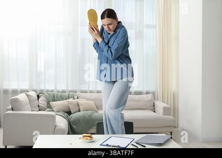 Giovane donna con la pantofola che guarda con disgusto gli scarafaggi sul tavolo bianco all'interno. Problema con i parassiti Foto Stock