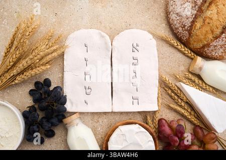 Happy Shavuot. Due pietre con dieci comandamenti in ebraico antico, cereali, latte e formaggio Foto Stock