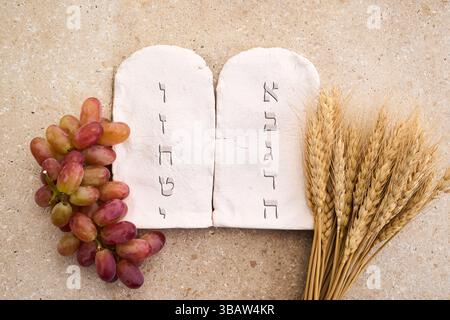 Happy Shavuot. Due pietre con dieci comandamenti in ebraico antico, cereali, latte e formaggio Foto Stock