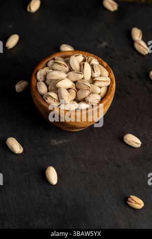 pistacchio nelle conchiglie con sale aggiunto, pistacchio non sbucciato fritto in una ciotola di legno con conchiglie fessurate, primo piano Foto Stock