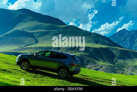 Auto moderna su una collina verde in una pittoresca valle di montagne, concetto di viaggio Foto Stock