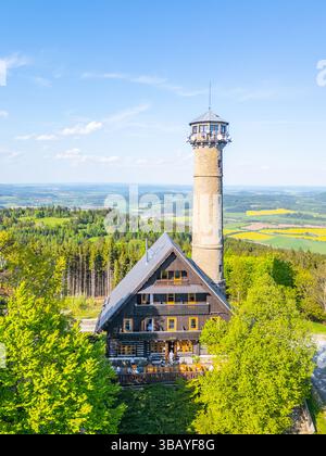 La prospettiva aerea cattura la torre di osservazione di Svatobor circondata da vegetazione lussureggiante e colline ondulate in Cechia, mostrando la bellezza panoramica della regione in una giornata limpida. Foto Stock
