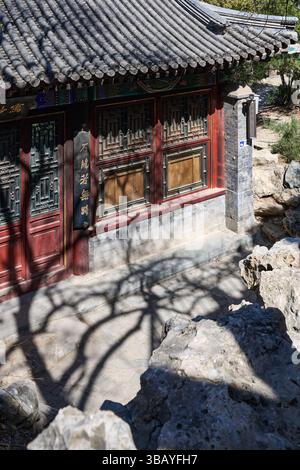 Un tranquillo sentiero in pietra conduce attraverso una foresta ombreggiata a un vecchio edificio cinese dalle mura rosse nascosto tra alberi e rocce Foto Stock