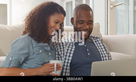Giovane coppia seduta sul pavimento nella lounge con un laptop insieme Foto Stock