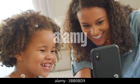 La madre si siede con la figlia a casa e porta Selfie sul cellulare Foto Stock