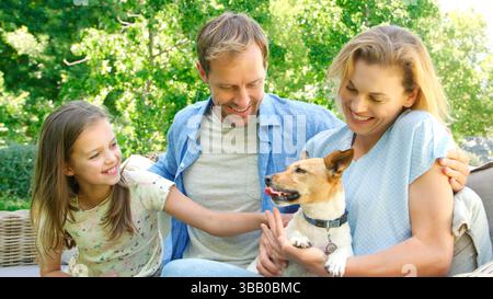 Famiglia sorridente seduta sul sedile all'aperto nel giardino estivo con cane Foto Stock