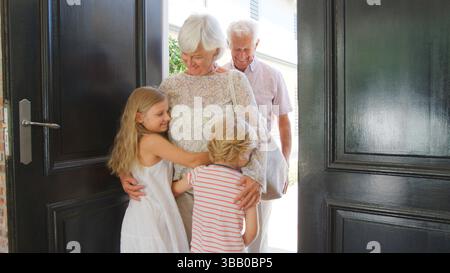 I nipoti salutano e abbracciano i nonni in visita alla porta d'ingresso Foto Stock