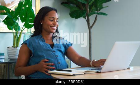 Donna americana incinta che usa il laptop al tavolo che lavora da Casa Foto Stock