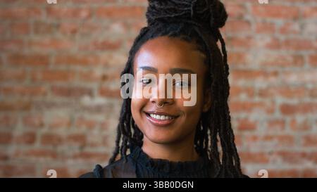 Ritratto di una donna afroamericana sorridente in piedi contro il muro di mattoni in Coffee Shop Foto Stock