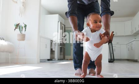 Primo piano del padre che incoraggia la figlia sorridente a fare i primi passi e camminare a casa Foto Stock