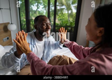 Giovani coppie diverse che sorridono gioiosamente insieme nel loro luminoso soggiorno, indossando abiti casual Foto Stock