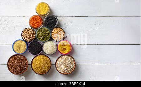 Varietà di cereali, legumi e pasta disposti in ciotole su sfondo bianco in legno. Copia spazio. Cereali assortiti, legumi e pasta in ciotole disposte Foto Stock