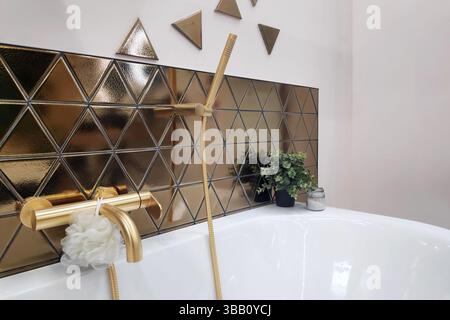 Bagno di design lussuoso e moderno, con piastrelle triangolari dorate, finiture in oro opaco e decorazioni minimaliste con un tocco di verde. Foto Stock