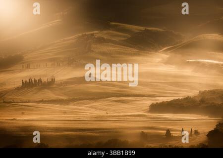 Calda luce dorata all'alba sulle colline della Val d'Orcia in Toscana, Italia, in una splendida mattinata con nebbia e nebbia. Foto Stock