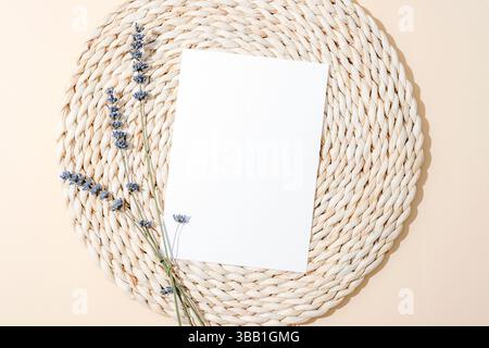Carta bianca bianca bianca con ciuffi di lavanda su un tappetino in paglia intrecciato. Vista dall'alto, posizione piatta, mockup. Foto Stock