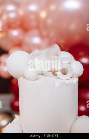 Torta bianca dolce per festeggiare il compleanno. Grande torta a due piani su uno sfondo di palloncini rossi. Squisita torta natalizia per la ragazza di compleanno. Foto Stock