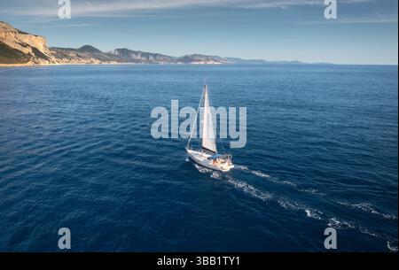 Vista aerea della barca a vela galleggiante e della costa rocciosa del mare nelle giornate di sole Foto Stock