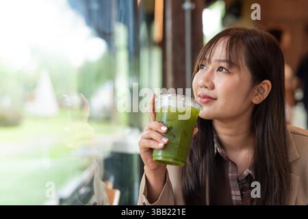 Giovane donna asiatica che beve succo verde detox in caffè Foto Stock