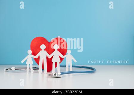 Una famiglia di ritagli di carta (quattro figure) in piedi davanti a un cuore rosso e uno stetoscopio, su sfondo blu con il testo "PIANIFICAZIONE FAMILIARE" sulla destra. Foto Stock