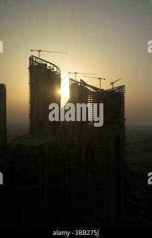 Costruzione di un nuovo edificio. Molte gru a grappolo e attrezzature per l'edilizia industriale contro il sole. silhouette gru edifici Foto Stock