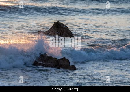 Le onde del mare colpiscono le rocce mentre il sole tramonta sulla costa inglese Foto Stock