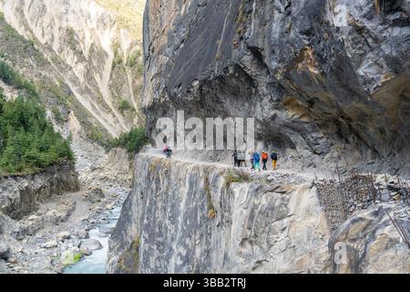 Gli escursionisti camminano lungo un suggestivo sentiero sulla scogliera tra Chame e Upper Pisang sul circuito dell'Annapurna, Nepal, con pareti di roccia verticali e profondo canyon Foto Stock