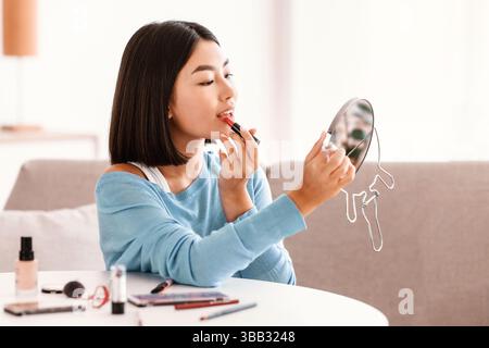 Asian Woman Recording il suo blog di bellezza, mettendo Lipstick rosso Foto Stock