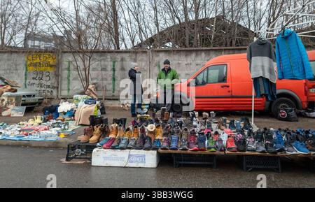 Kiev, Ucraina - 27 febbraio 2025: I venditori ambulanti interagiscono con i clienti in un vivace mercato delle pulci, presentando vari articoli di calzature e abbigliamento mentre la vita quotidiana si svolge intorno a loro. Foto Stock