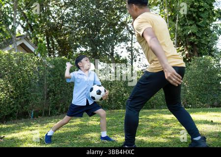 Attività: Padre e figlio giocano a calcio in giardino, godendo del tempo di qualità insieme. Foto Stock