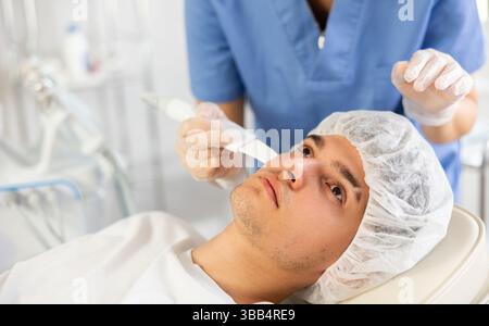 Giovane cosmetologa che fa esfoliazione al giovane uomo Foto Stock