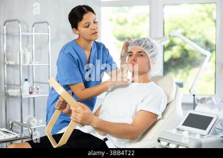 Giovane cosmetologa che esamina il volto di un giovane uomo Foto Stock