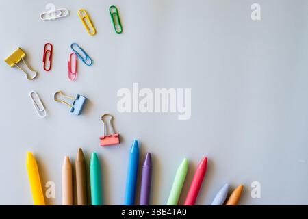 Disposizione piatta di penne colorate, graffette e graffette sparse su sfondo grigio chiaro che simboleggiano la creatività giocherellona le forniture scolastiche luminose Foto Stock
