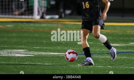 Un giovane atleta manovra abilmente la palla su un campo sintetico di notte. Foto Stock