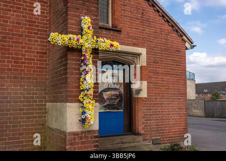 Una croce decorata con fiori colorati accanto a un cartello Coffee & Cake all'esterno della chiesa di St Andrews lungo il viale a Southampton, Inghilterra, Regno Unito Foto Stock