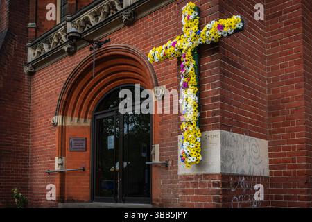 Croce cristiana decorata con fiori colorati per Pasqua all'esterno della chiesa di St Andrews lungo il viale di Southampton, Inghilterra, Regno Unito Foto Stock