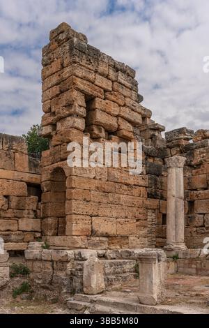 La porta bizantina sulla strada colonnata di Hierapolis presenta un arco di pietra e pareti parziali, con rovine e erba intorno. Foto Stock