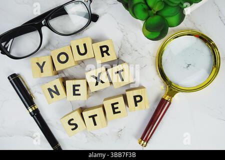 Il tuo prossimo passo con blocchi di legno lettere alfabetiche e vetro ingrandente su sfondo in marmo Foto Stock