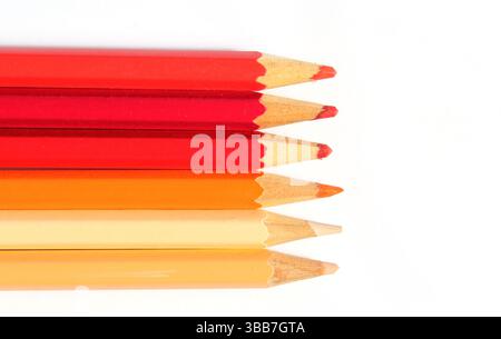 Fila di matite rosse, arancioni e gialle su sfondo bianco Foto Stock