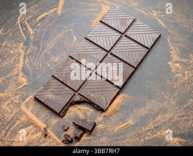 Barretta di cioccolato con un boccone nell'angolo con polvere di cioccolato intorno Foto Stock