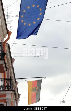 Le bandiere della Germania e dell'Unione europea sono appese su paletti contro il cielo blu e la facciata dell'edificio Foto Stock