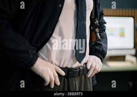 Persona che indossa i guanti in piedi in un ambiente d'ufficio moderno con computer e vari gadget in background Foto Stock