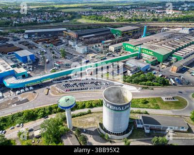 15 maggio 2025, Sassonia, Riesa: Veduta dell'Elba-Stahlwerke Feralpi. Le acciaierie di Riesa si concentrano su tecnologie più rispettose del clima con un nuovo laminatoio. Lo stesso giorno è stato inaugurato un nuovo laminatoio, che produce acciaio nel cosiddetto "ambito 1" senza emissioni dirette di CO2. In totale, Feralpi ha investito più di 220 milioni di euro nel sito - secondo l'azienda, il più grande investimento singolo nella sua storia tedesca. L'espansione creerà circa 100 nuovi posti di lavoro, portando la forza lavoro a circa 950 dipendenti. (Vista aerea con drone) foto: Jan Woitas/dpa Foto Stock