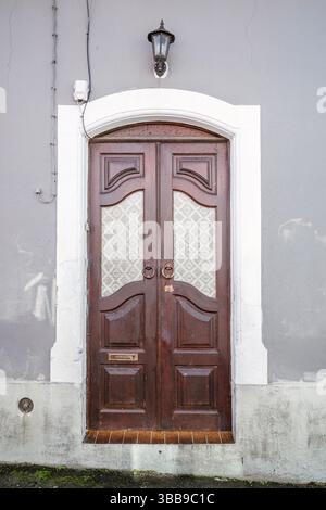 Doppia porta in legno con telaio ad arco. Incantevole vista di una doppia porta in legno scuro con pannelli decorativi in vetro e maniglie rotonde in metallo Foto Stock