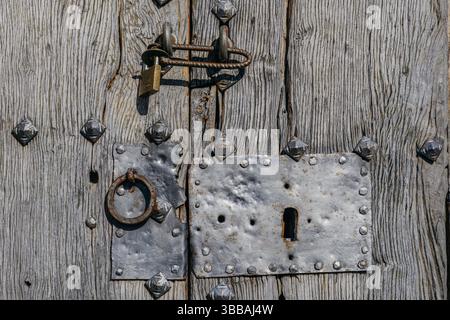 Antica porta ad arco in legno con borchie in metallo nello storico edificio in pietra. Ingresso tradizionale con accessori in ferro battuto e buca per serratura in taglio grezzo Foto Stock