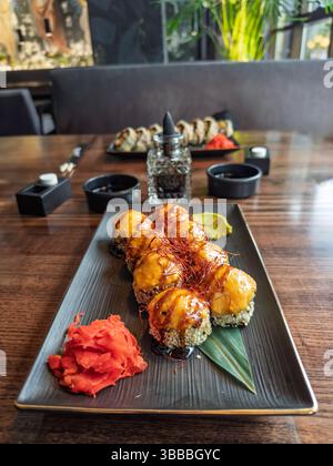 Piatto gourmet di sushi Rolls al forno con zenzero e wasabi nel ristorante. Appetitosi sushi Rolls al forno con salsa e sesamo, serviti con condimenti. Foto Stock