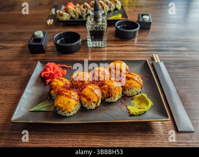 Cucina Giapponese: Delizioso sushi al forno su un tavolo di legno del ristorante. Appetitosi panini di sushi al forno con condimenti, zenzero e Wasabi. Foto Stock