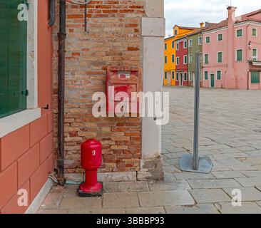 Venezia, Italia - 10 gennaio 2017: Red Fire Hydrant and Post Box presso Brick Wall Colourful Houses Town Square a Burano Island Winter Day Travel. Foto Stock