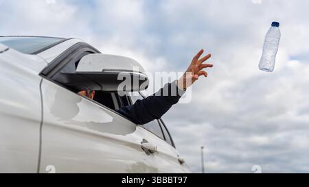 Un uomo che getta una bottiglia d'acqua di plastica usata fuori dalla sua auto e inquina l'ambiente. Foto Stock
